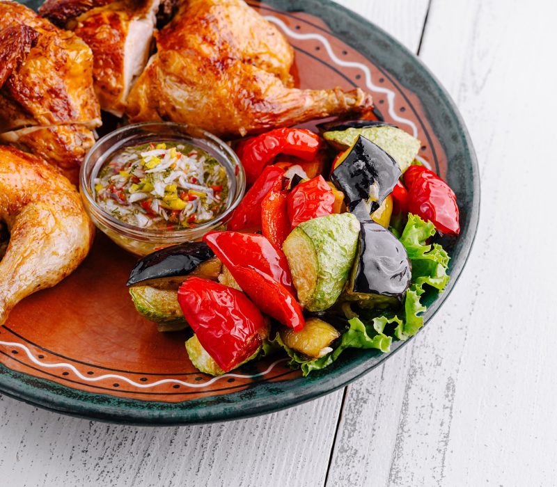 Delicious roasted chicken served on a plate with grilled vegetables and sauce
