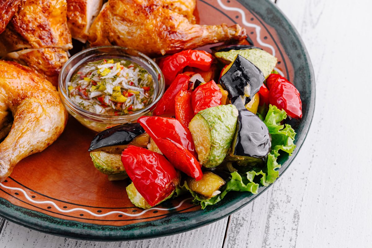 Delicious roasted chicken served on a plate with grilled vegetables and sauce